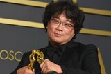 Bong Joon Ho makes his two Oscar statues kiss at the Academy Awards ceremony.