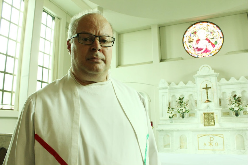 Father Andrew Hayes stands in front of an alter.