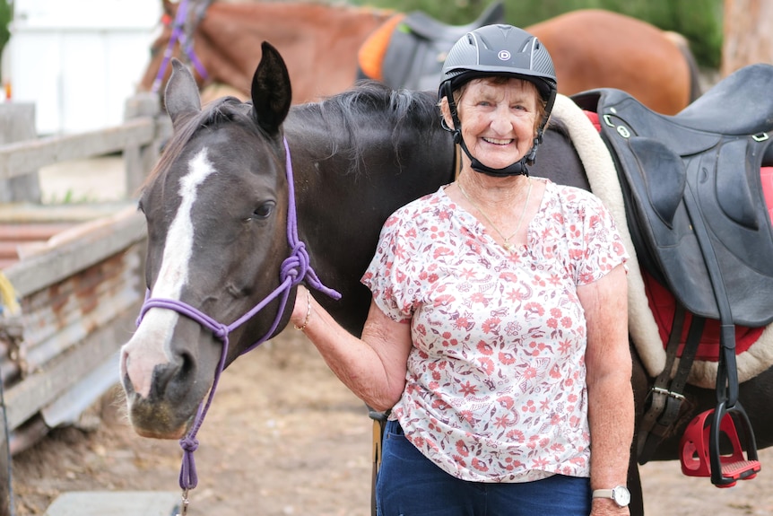 An older lady stands next to a black horse. 