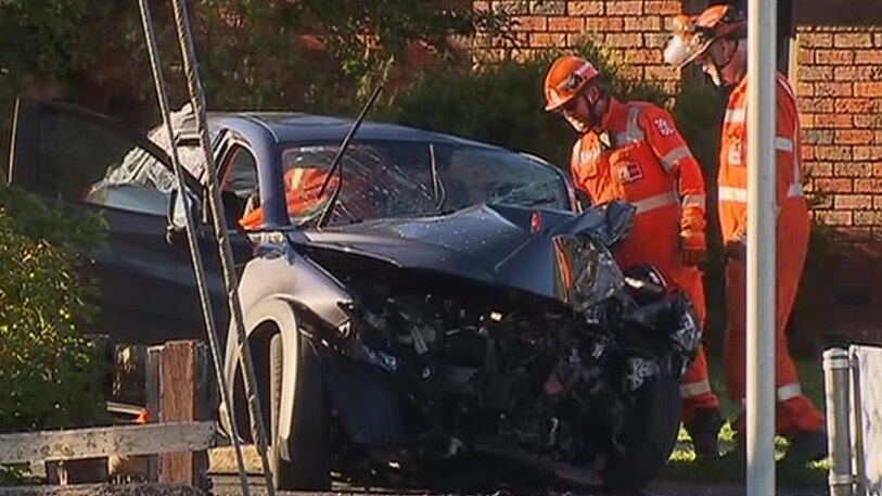 Two men wearing orange SES overalls inspect a black car with a crushed bonnet.