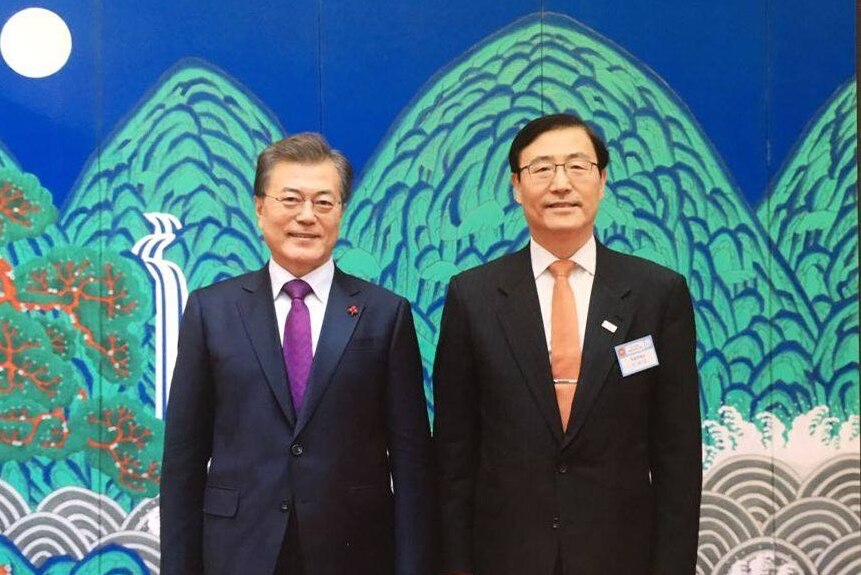 Lee Baeksoon and Moon Jae-in stand next to each other in front of a mural of mountains and the sea.