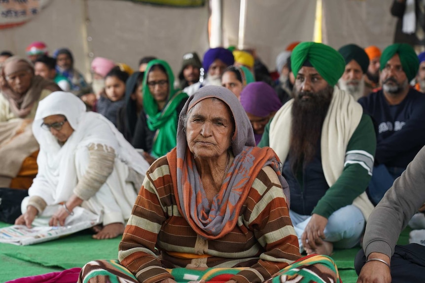 a woman sits on the ground in front of others sitting on the ground in a tent