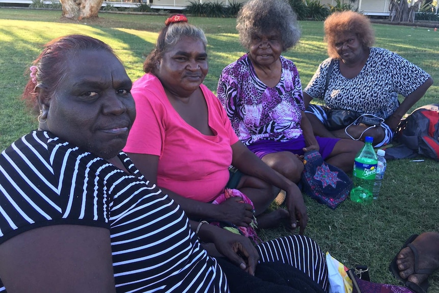 Four Aboriginal women sit side-by-side on Male Oval in Broome looking at the camera.