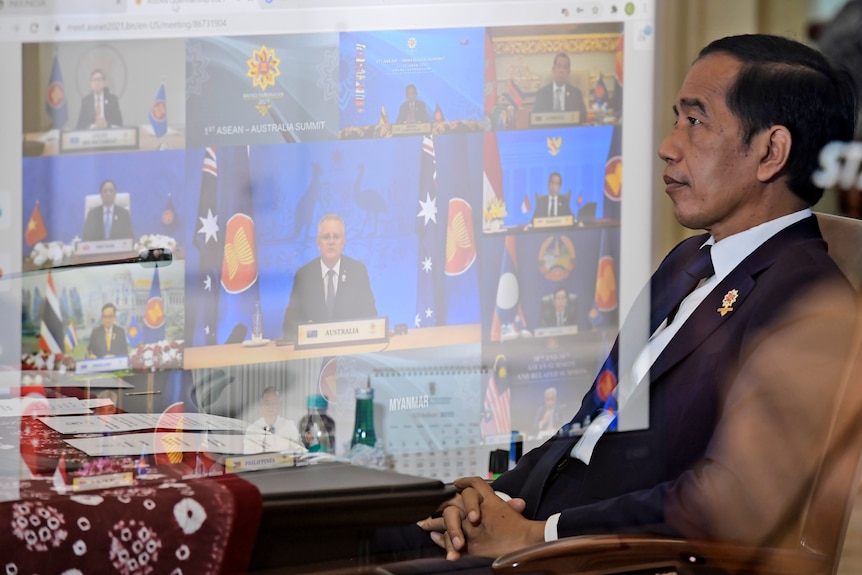 Joko Widodo sitting back in a chair with a projection of ASEAN virtual meeting