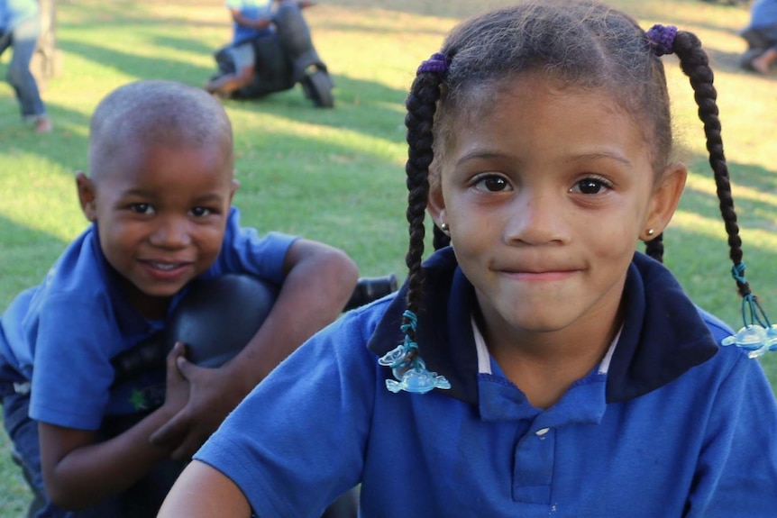 A young African boy and girl wearing blue school shirts.