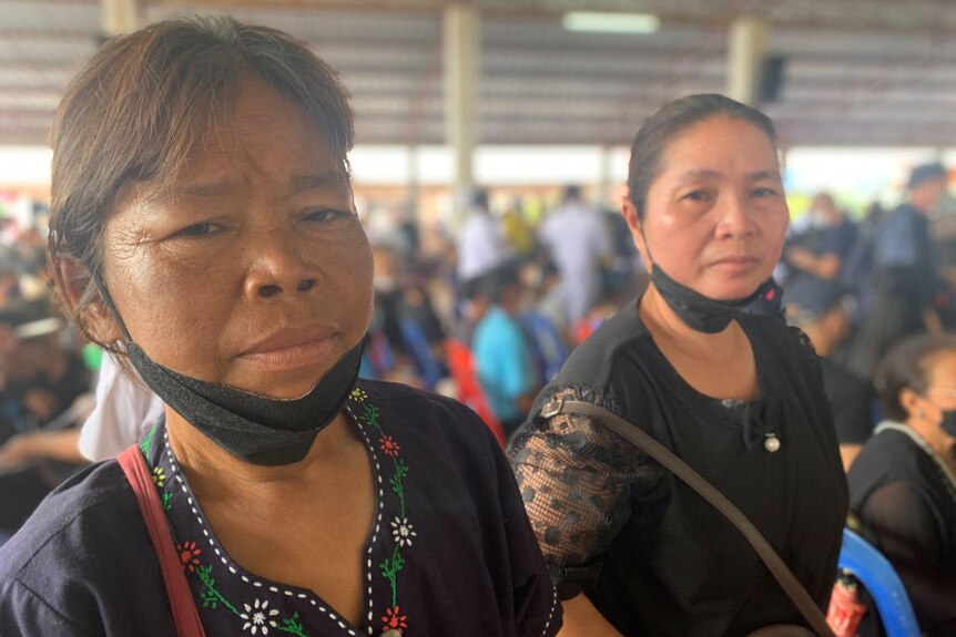 A woman's eyes are red and filled with tears as she looks towards camera in a hall full of people