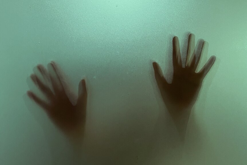 A spooky image of blurry hands raised as if against glass  