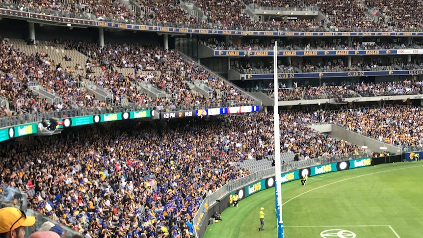 A wideshot of Perth Stadium during an AFL game with pockets of empty seating.