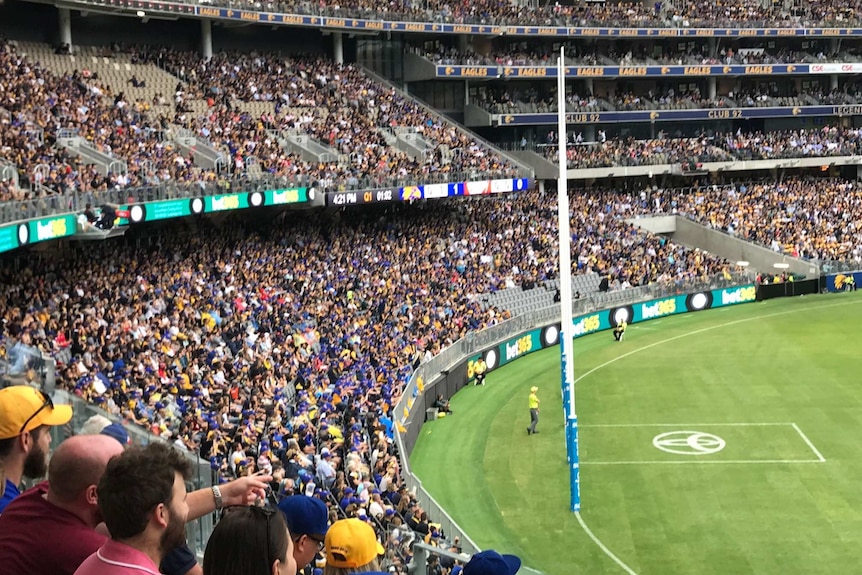 A wideshot of Perth Stadium during an AFL game with pockets of empty seating.