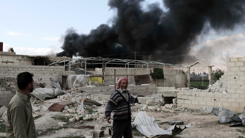 A Syrian man stands in front of billowing smoke after reported air strikes on the outskirts on Damascus