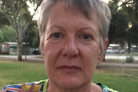 A woman in a caravan park stares unsmiling at the camera