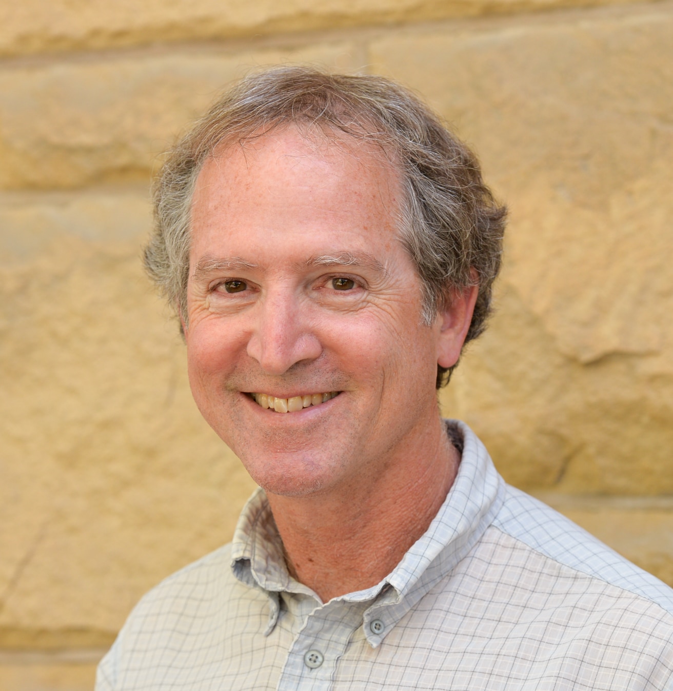 Photo portrait of a man in a button-down shirt smiling at the camera.