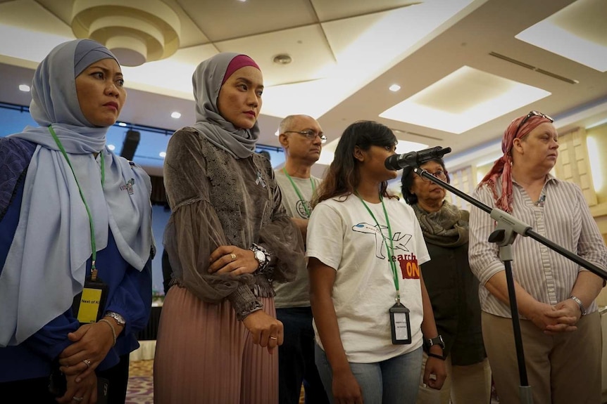 A group of unhappy people stand together in front of a microphone.