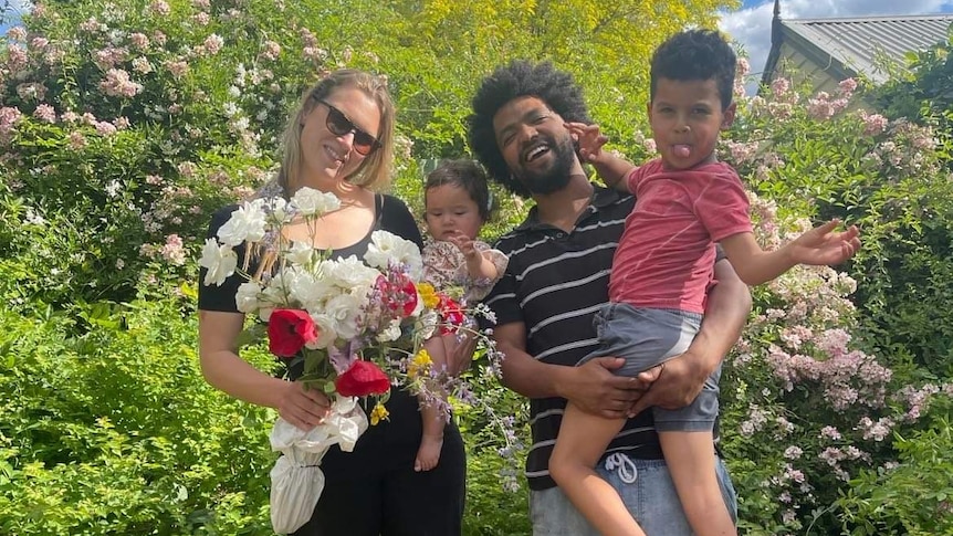 Jessica Fairfax holds flowers, standing with her partner and two small children