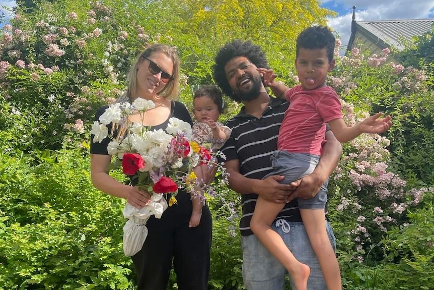 Jessica Fairfax holds flowers, standing with her partner and two small children