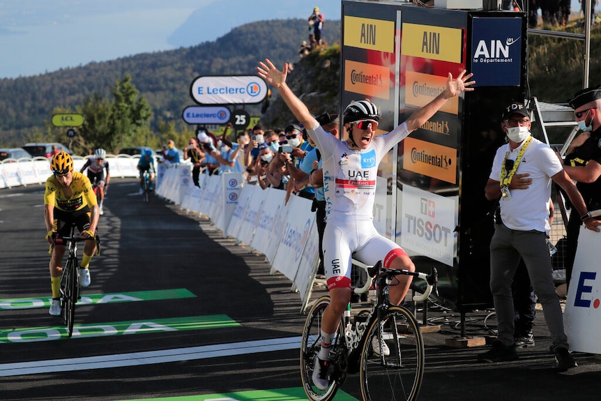 A cyclist wearing a white jersey throws his arms in the air while crossing the finish line of a stage on the Tour de France.