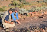 Two scientists point at outback rocks.