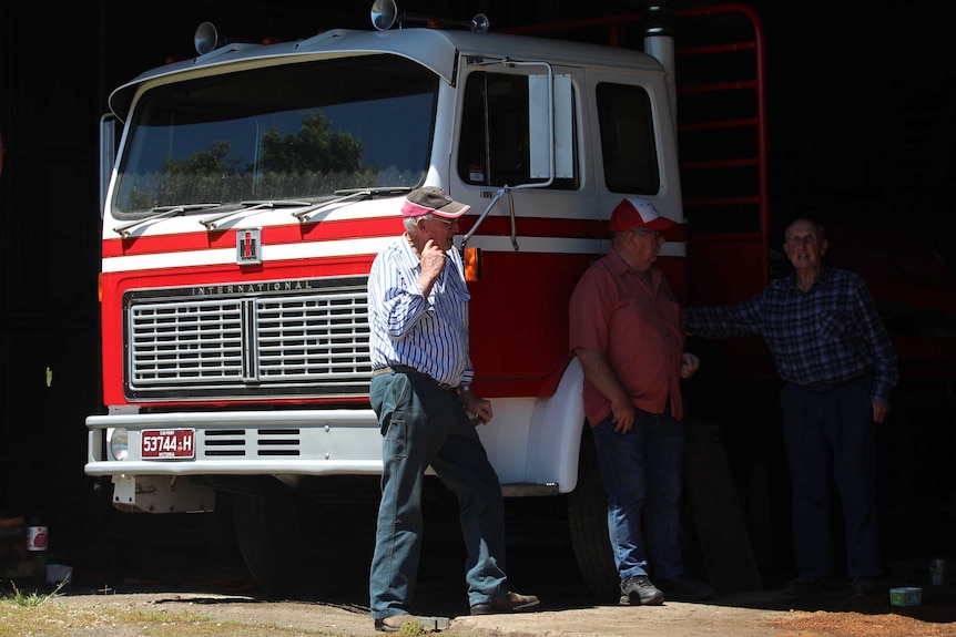 Three men stand with a vintage truck in a shed