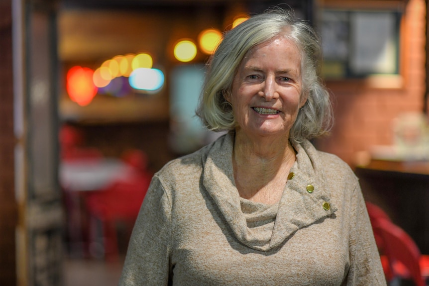 Lady with white hair smiles at camera while wearing a beige coloured jumper