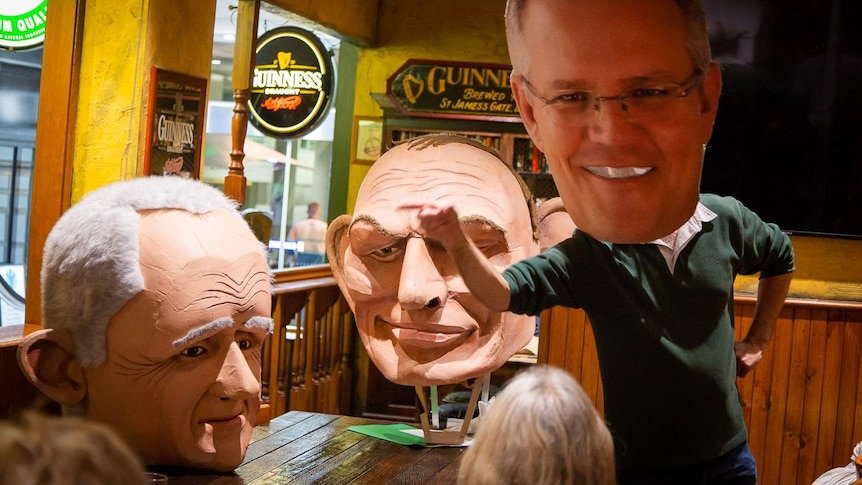 A Scott Morrison mask is waving next to giant Tony Abbott and Malcolm Turnbull masks