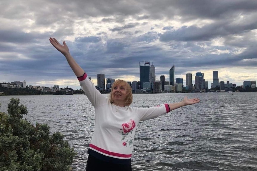 a woman stands in front of a city skyline smiling and throwing her arms in the air.