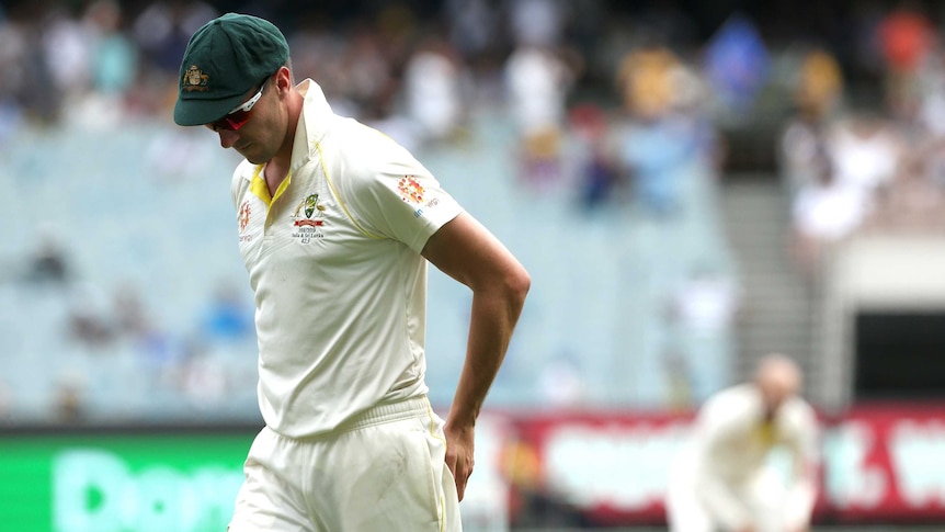 Australia fielder Pat Cummins looks down with his hands on his posterior as Nathan Lyon, blurred in the background, looks on.