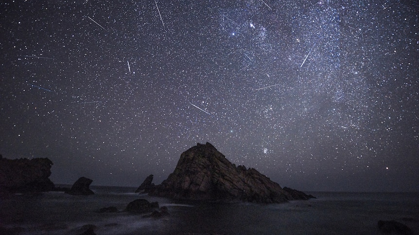 Meteor shower over ocean and rocks