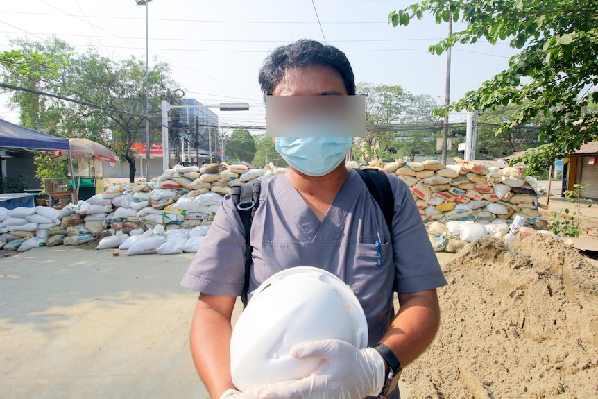 A man in Myanmar wearing glasses a face mask and carrying a helmet 