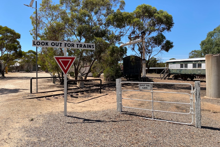 A gate and a sign that says look out for trains in a rural setting