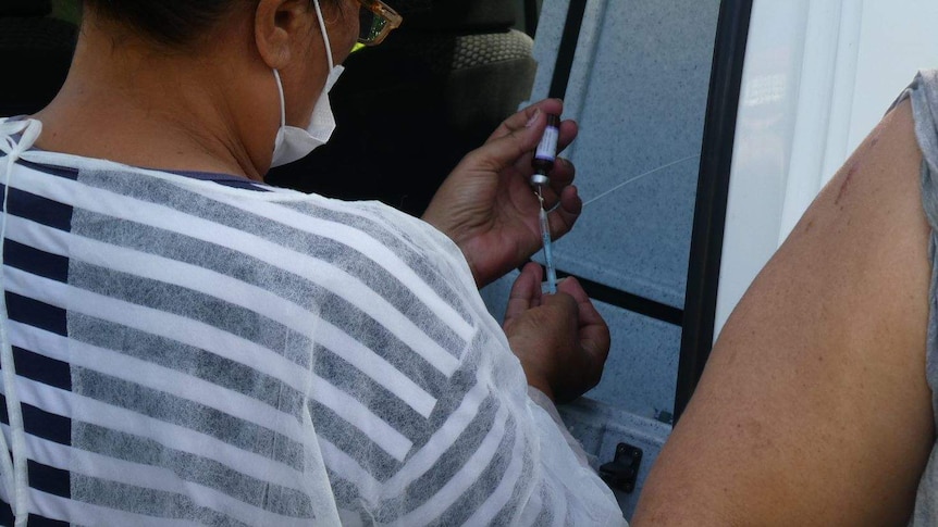 A healthcare officia holds a needle while theyl prepare to immunise somebody against measles.