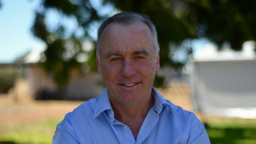 a close u head shot of tim, who has short grey hair and is staring directly into the lens. he's wearing a blue shirt.