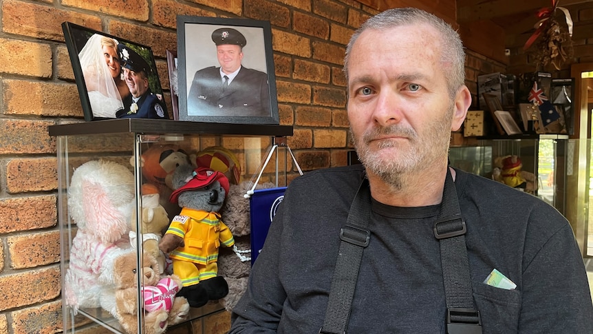 A former firefighter standing in his home, with family photos behind him.