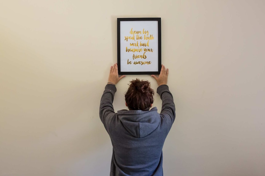 A woman adjusts a framed quote hanging on a wall.