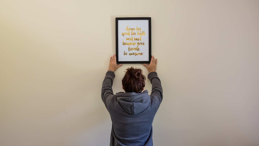 A woman adjusts a framed quote hanging on a wall.