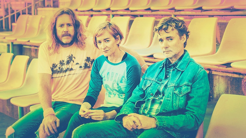 Three members of Spiderbait sit side-by-side in a grandstand