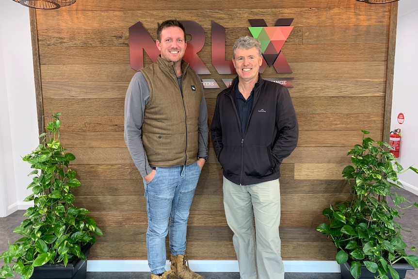 Two men standing and smiling in front of an NRLX sign in an office.