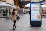 A woman with her back to the camera walks towards a COVID-19 vaccination sign on a billboard in Yagan Square in Perth.