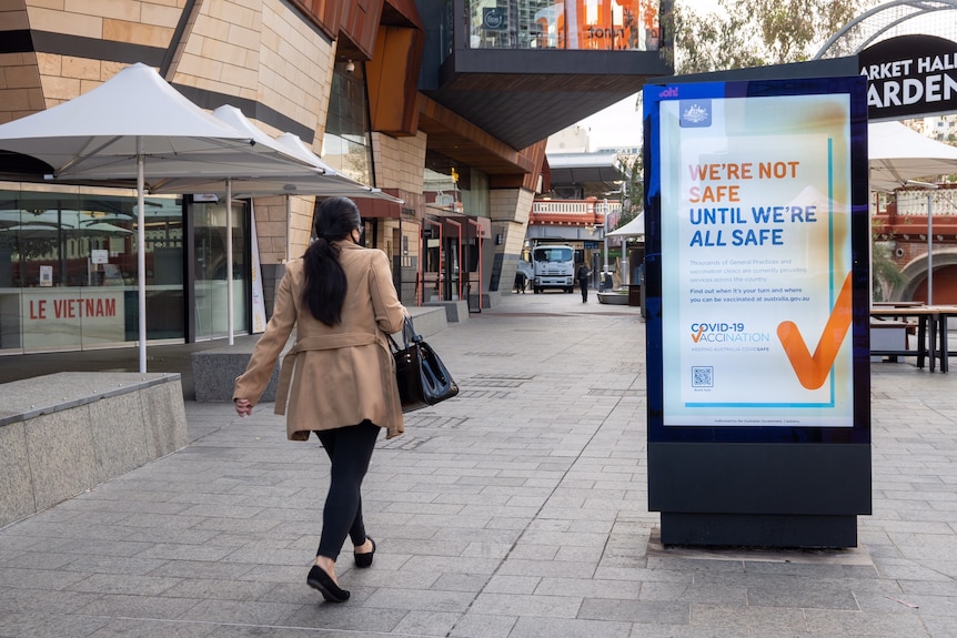 A woman with her back to the camera walks towards a COVID-19 vaccination sign on a billboard in Yagan Square in Perth.