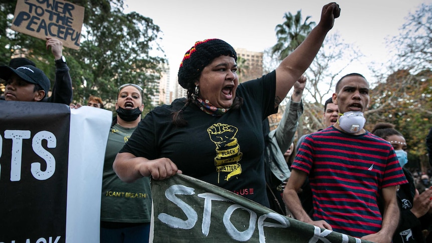 A woman wearing a hat and black lives matter shirt raises her left fist.