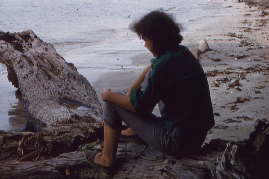 A woman sitting on a rock with a tropical beach in the background.