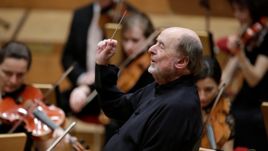 A man leans back in a chair while conducting an orchestra. 