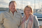 A man and a woman standing next to each other with boats in the background