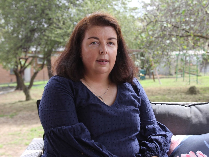 A woman with shoulder length brown hair sitting in a park with the background out of focus.