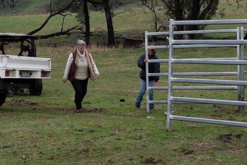 a woman lifts a large steel gate to shut it, while another woman is moving to help her.