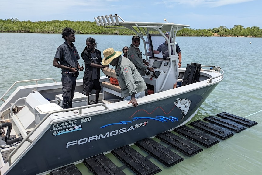 Traditional Owners and rangers standing up on a boat above a line of Oysters baskets full of spats near Dorcherty Island.