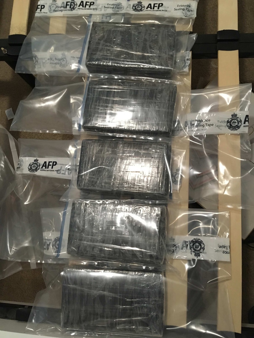 Five bricks of cocaine wrapped in black plastic, sealed in individual evidence bags lined up on a table.