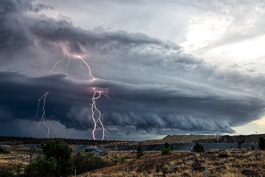 Storm front moving towards a hill with a flash of lightning