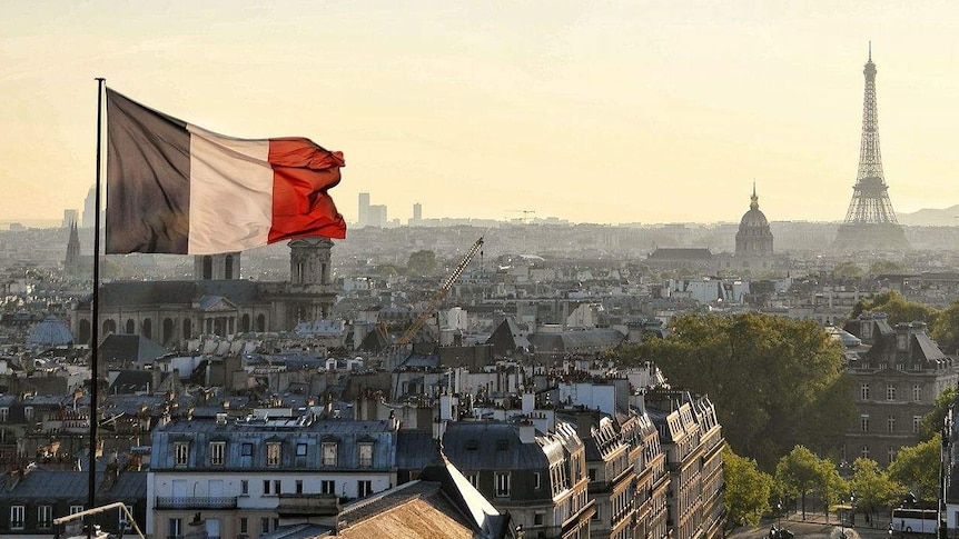 A French flag flying above the city during sunset. The eiffel tower and Cathedrale de la Sainte-Trinite are in the background