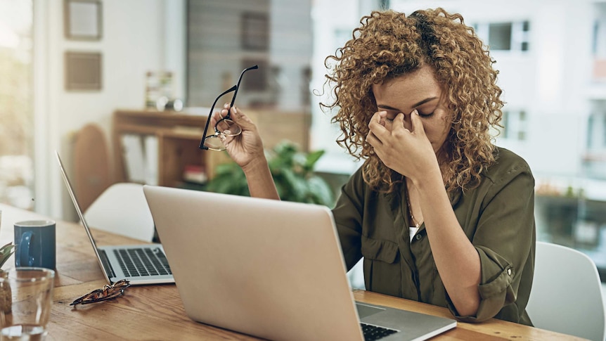 A young woman suffering from stress holds her head while using a computer at her work desk.