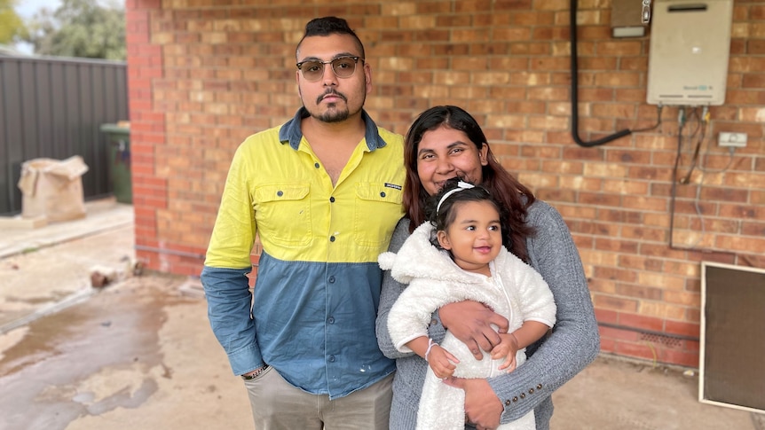 A man in a tradie top standing next to a woman holding an eight-month old baby girl